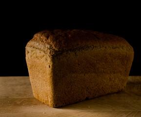 Loaf of black rye bread, in the shape of a brick on a wooden board on a black background