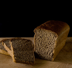 Loaf of black rye bread, cut into pieces, in the shape of a brick on a wooden board on a black background