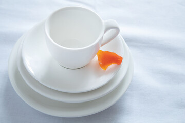 Small white cup on several white plates / saucers on a light background close-up