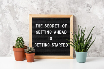 The Secret Of Getting Ahead Is Getting Started. Motivational quote on letter board, cactus, succulent flower on white table. Concept inspirational quote of the day. Front view