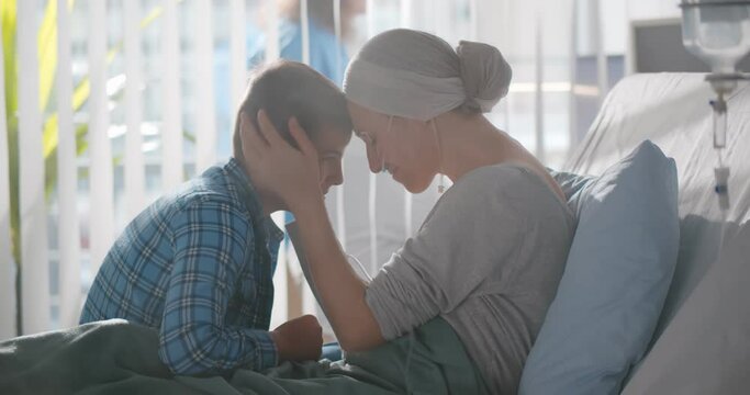 Upset teenage boy embracing sick mother with cancer in hospital