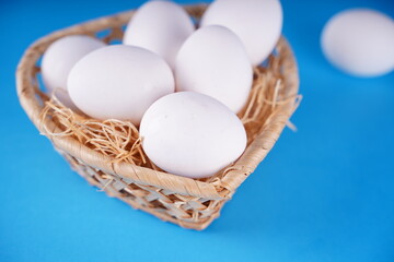 Farm raw, fresh white chicken egg in a basket on a blue background. Concept: a fresh egg for the morning breakfast.