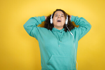 Young african american girl wearing gym clothes and using headphones relaxing and stretching, arms and hands behind head and neck smiling happy