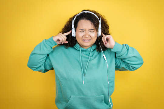 Young african american girl wearing gym clothes and using headphones covering ears with fingers with annoyed expression for the noise of loud music. Deaf concept.