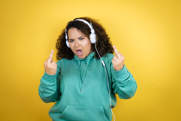 Young african american girl wearing gym clothes and using headphones showing middle finger doing...