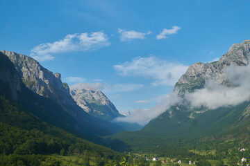 Fototapeta na wymiar View on beautiful valley in Montenegro with mountains, clouds, blue sky, forests and some houses