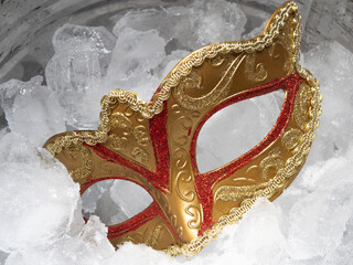 Traditional golden carnival Venetian mask with red ornaments in a bucket with crushed ice cubes. Brazilian Mardi Gras Festival. The concept of a hot parade, masquerade.