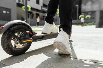 female foot in white sneakers are riding electric scooter in urban background