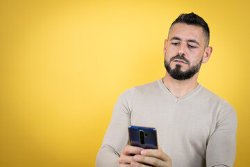 Handsome man with beard wearing sweater over yellow background texting with her phone