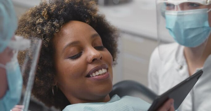Close up of dentist and assistant showing tablet computer to woman patient at dental clinic office