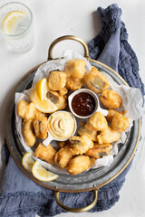 Overhead view of a delicious hake tempura over a circular tray with curry and bbq sauces in the middle.