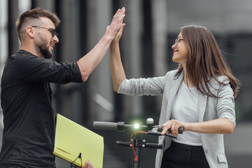 Young couple on vacation having fun driving electric scooter through the city. Giving high five.