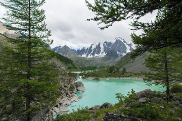 Fototapeta na wymiar The pearl of the Altai Mountains, the upper lake Shavlo, above which rise three glacier-covered peaks-A fairy tale, a Dream and a Beauty. The water in the lake has an amazing turquoise color