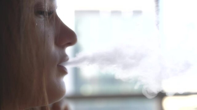 the girl smokes the vape blows smoke from her mouth in slow motion