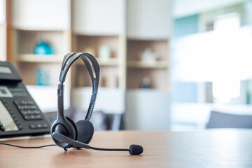 Obraz premium Close up soft focus on headset with telephone devices at office desk for customer service support.VOIP headset for customer service support (call center) concept.