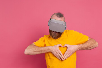Handsome bearded man in vr glasses shows heart with hands studio background