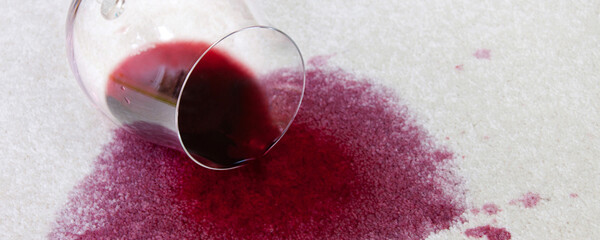 Umgestoßenes Weinglas mit Rotwein auf Teppich