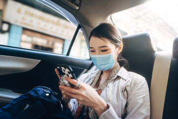 Young adult asian woman with face mask for public health in taxi car using mobile phone. - obrazy, fototapety, plakaty