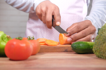 young man cutting fresh carrots on chopping board on table 
