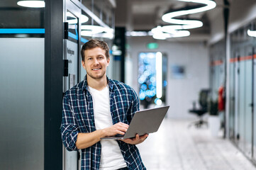 Caucasian guy freelancer with laptop. A successful guy dressed in stylish casual wear stands in a...