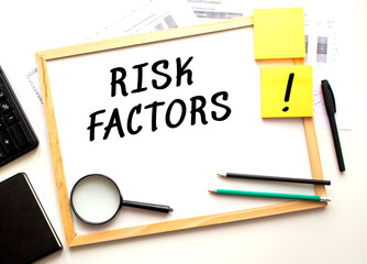 RISK FACTORS text is written on a white office board. Work table with office supplies.