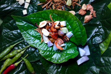 Miang Kham Small pieces of garnish are arranged on basil leaves. Contains ginger, lime, roasted coconut, onions, dried shrimp and peanut lad. Was placed on the basil leaves.