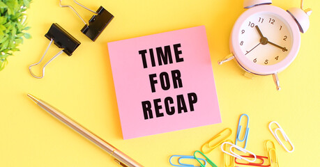 Pink paper with the text TIME FOR RECAP. Clock, pen on a yellow background.