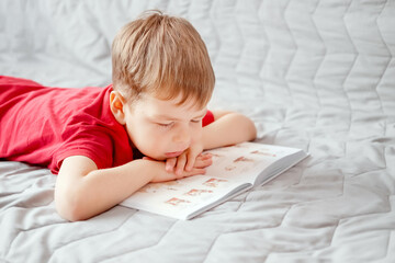 home schooling. Boy reads a book while lying on the bed. Book reading time. Child development....