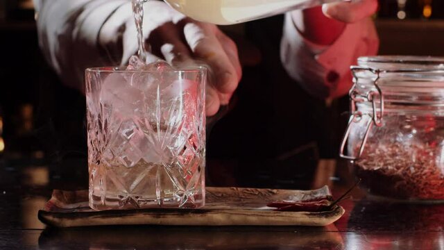 Bartender preparing a fancy, fresh drink in a cocktail bar. Man pouring liquor into a crystal glass, luxurious restaurant serving expensive alcohol.