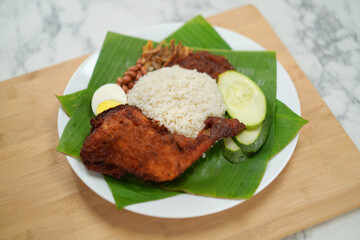 Nasi Lemak dish with chicken drum stick on marble surface with coconut leaf