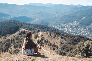 Naklejka na ściany i meble Young woman sitting on a rock with backpack and looking to the horizon