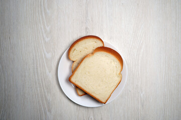 Two slices of bread on white plate on white wooden verneer background