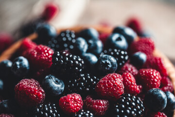 Ripe blackberries with leaves in a bowl on a wooden board on a dark background