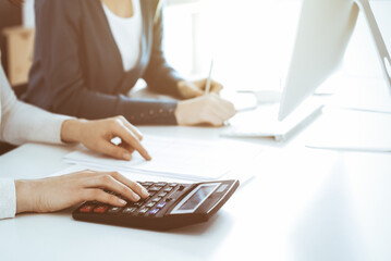 Accountant checking financial statement or counting by calculator income for tax form, hands close-up. Business woman sitting and working with colleague at the desk in office. Audit concept
