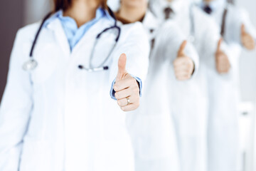 Group of modern doctors standing as a team with thumbs up in hospital office. Medical help, insurance in health care, best desease treatment and medicine concept