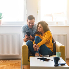 Smiling couple looking in smartphone together at home.
Beautiful loving couple laughing and...