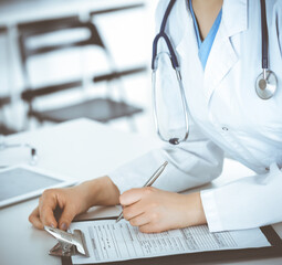 Unknown woman-doctor or internal student filling up medical documents while standing in clinic reception desk. Data in medicine