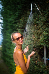 Beautiful young woman taking a shower outdoors. Attractive young woman in yellow one-piece enjoys...