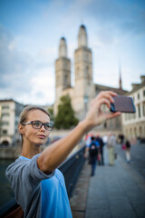 Pretty, female tourist taking selfies in front of the Grossmunster Church in Zurich, Switzerland