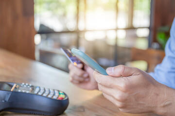 Man holding smartphone and credit card with a credit card reader machine at bar counter, Hand of customer paying with contactless credit card with NFC technology.
