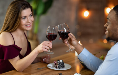 Happy interracial couple with glasses of red wine having date in restaurant