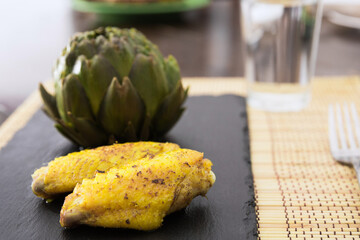 cooked fried chicken wings and halves artichokes on black stone plate