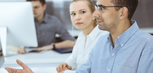 Business people working together in modern office. Happy smiling adult businessman using pc computer with colleagues. Teamwork and partnership concept