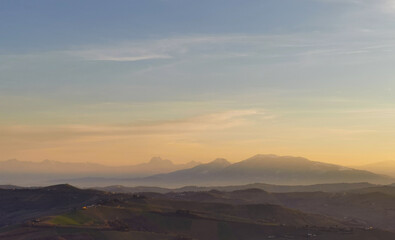 Fototapeta na wymiar Montagne e valli dell’Appennino in un tramonto di luce e foschia azzurro e arancio