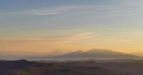 Naklejka premium Montagne e valli dell’Appennino in un tramonto di luce e foschia azzurro e arancio