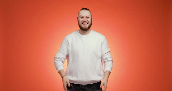 Smiling guy approving nodding head.Emotional bearded young man with tail on his head. Advertising concept. Man in white sweater points hands aside and pretends he gives something on red background.