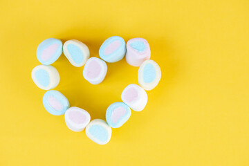 Multicolored sweet soft marshmallow in the shape of a heart on a yellow background. Valentines day card