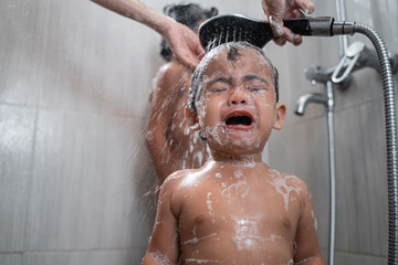the baby cries with a face full of foam while taking a shower with copyspace in the bathroom