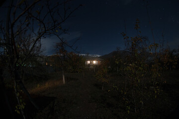Fototapeta premium Mountain night landscape of building at forest at night with moon or vintage country house at night with clouds and stars. Summer night.