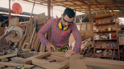 Worker man carpenter in factory using chainsaw machine cutting piece of wood product. smart man wearing glasses to protect saw dust from wood. craftsman working in wood workshop industrial.
